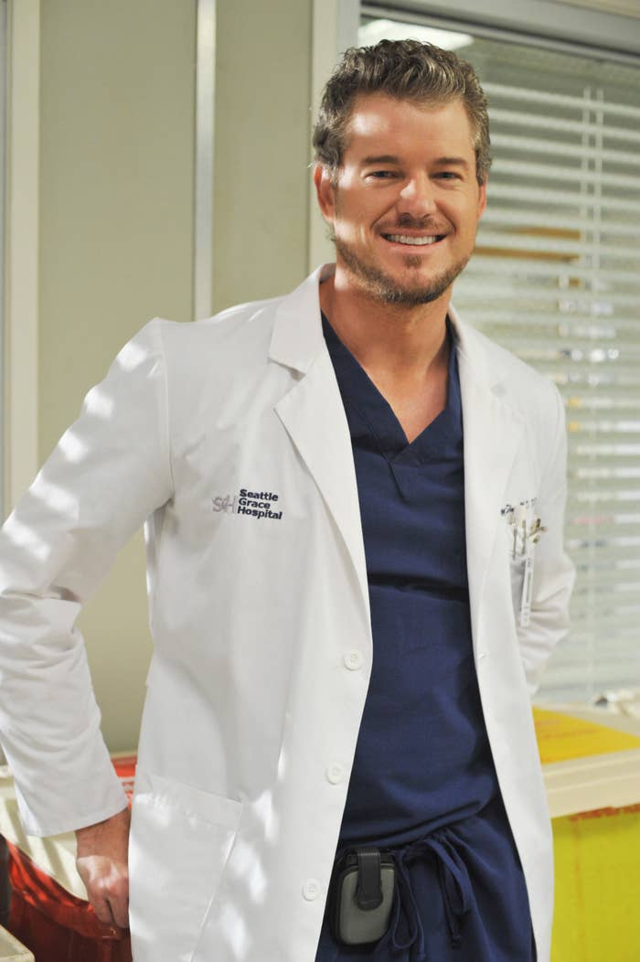A idiosyncratic   wearing a bluish  scrub apical  and a achromatic  laboratory  overgarment  with &quot;Seattle Grace Mercy West Hospital&quot; connected  the chest. The idiosyncratic   is smiling and lasting  indoors