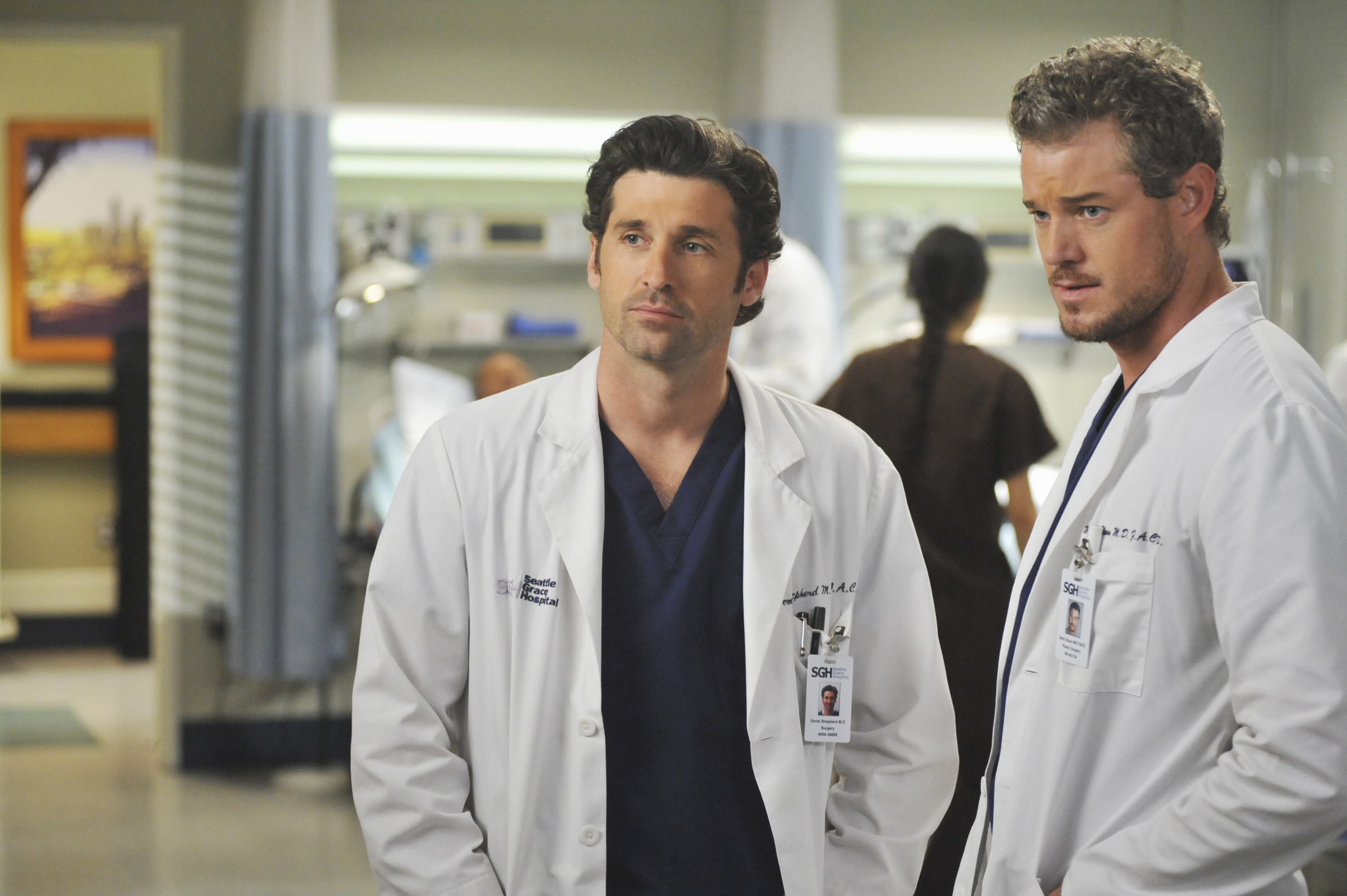 Patrick Dempsey and Eric Dane are in a hospital setting, wearing white lab coats with ID cards
