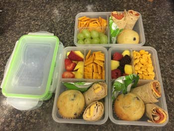 reviewer's four neatly arranged meal prep containers with wraps, grapes, muffins, crackers, fruits, and cheese snacks
