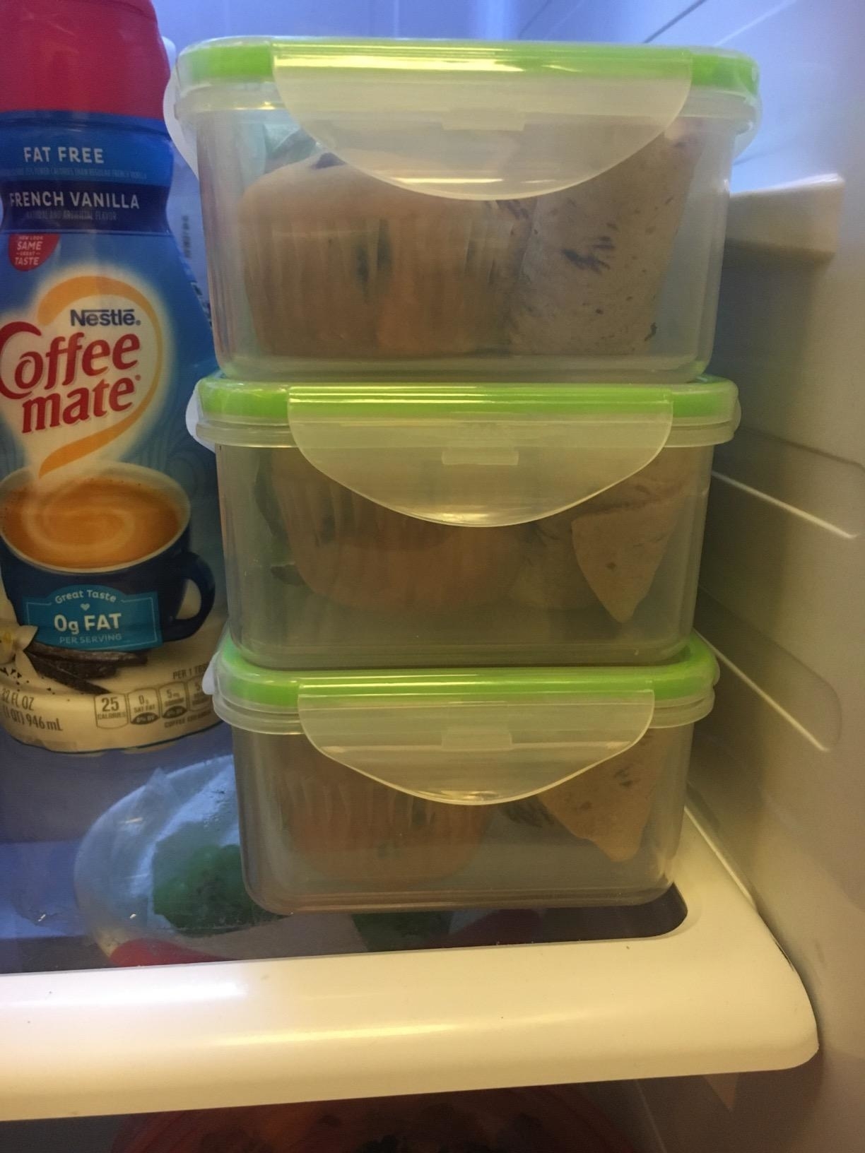 reviewer's three plastic containers stacked in a fridge, each containing muffins. Coffee-mate creamer and other grocery items are visible beside the containers