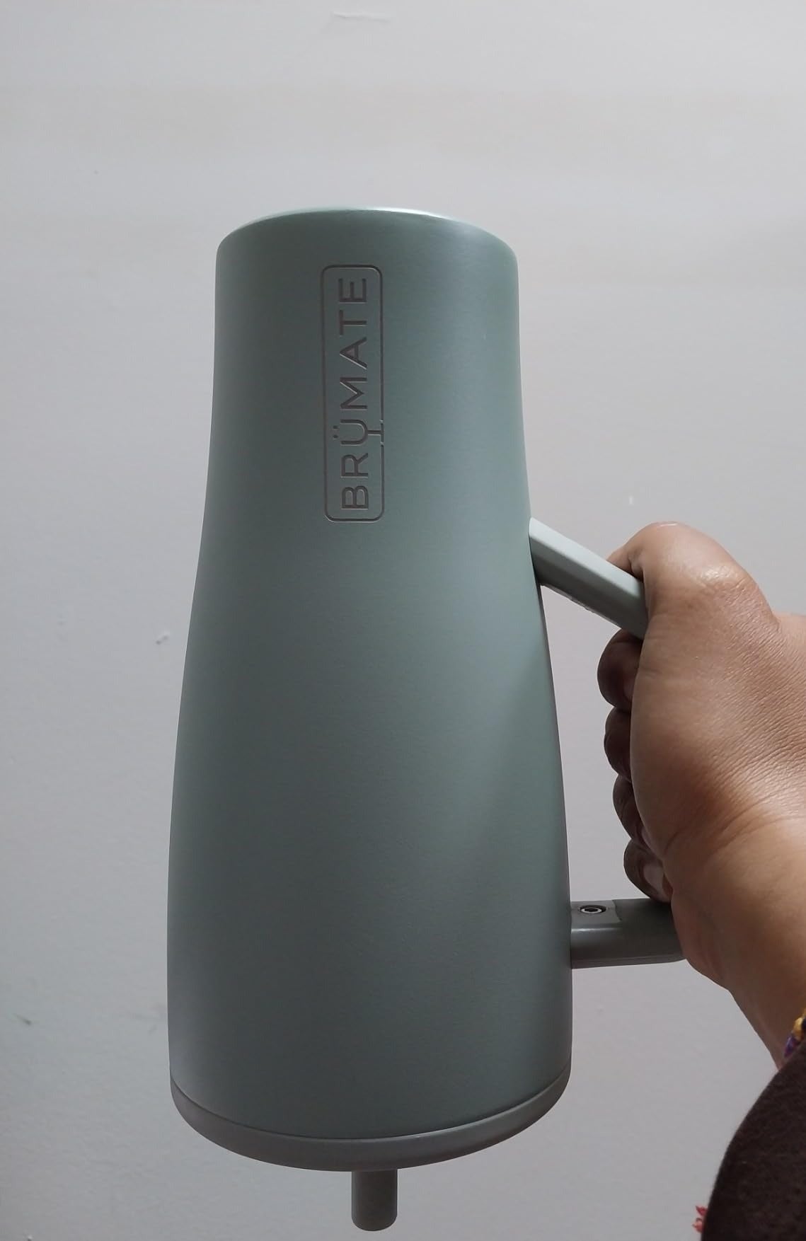 Hand holding a BrüMate java  mug with a sleek, modern   design, showcasing the brand's logo connected  the side