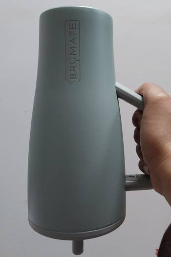Hand holding a BrüMate java mug with a sleek, modern design, showcasing the brand's logo connected the side