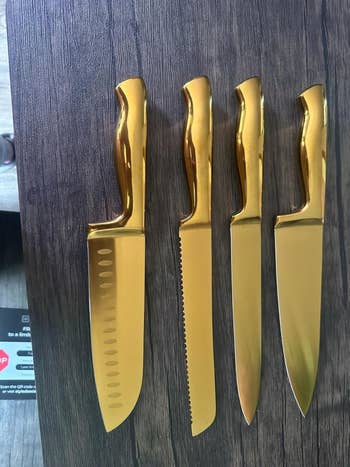 reviewer's set of four gold kitchen knives with different blade styles displayed on a wood surface