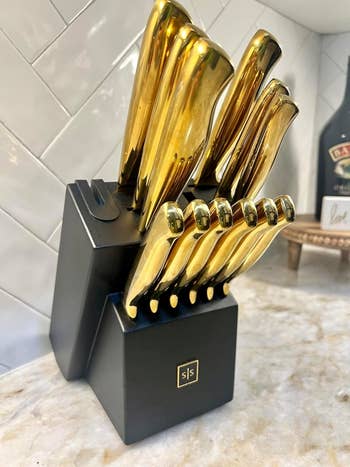 reviewer's black knife block holds a full set of shiny gold kitchen knives, neatly organized on a kitchen counter