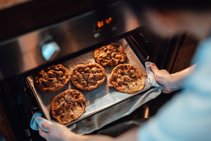 A person takes a baking tray of freshly baked chocolate chip cookies out of an oven