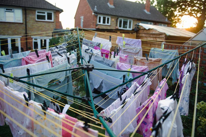 Clothes are hanging on a rotary washing line in a backyard with houses in the background. The scene captures daily domestic life