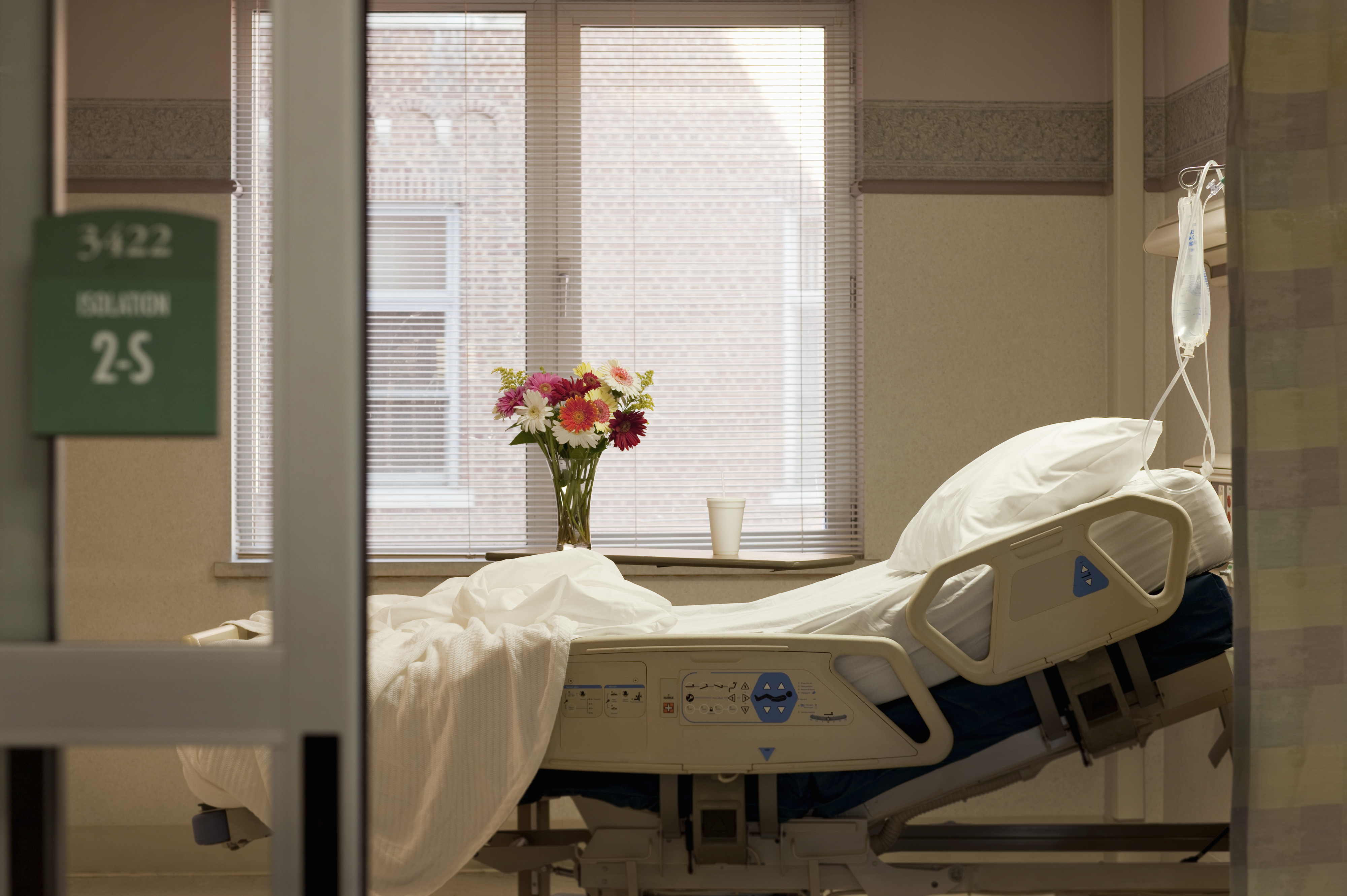 An empty hospital bed with a bouquet of flowers on the windowsill in a hospital room