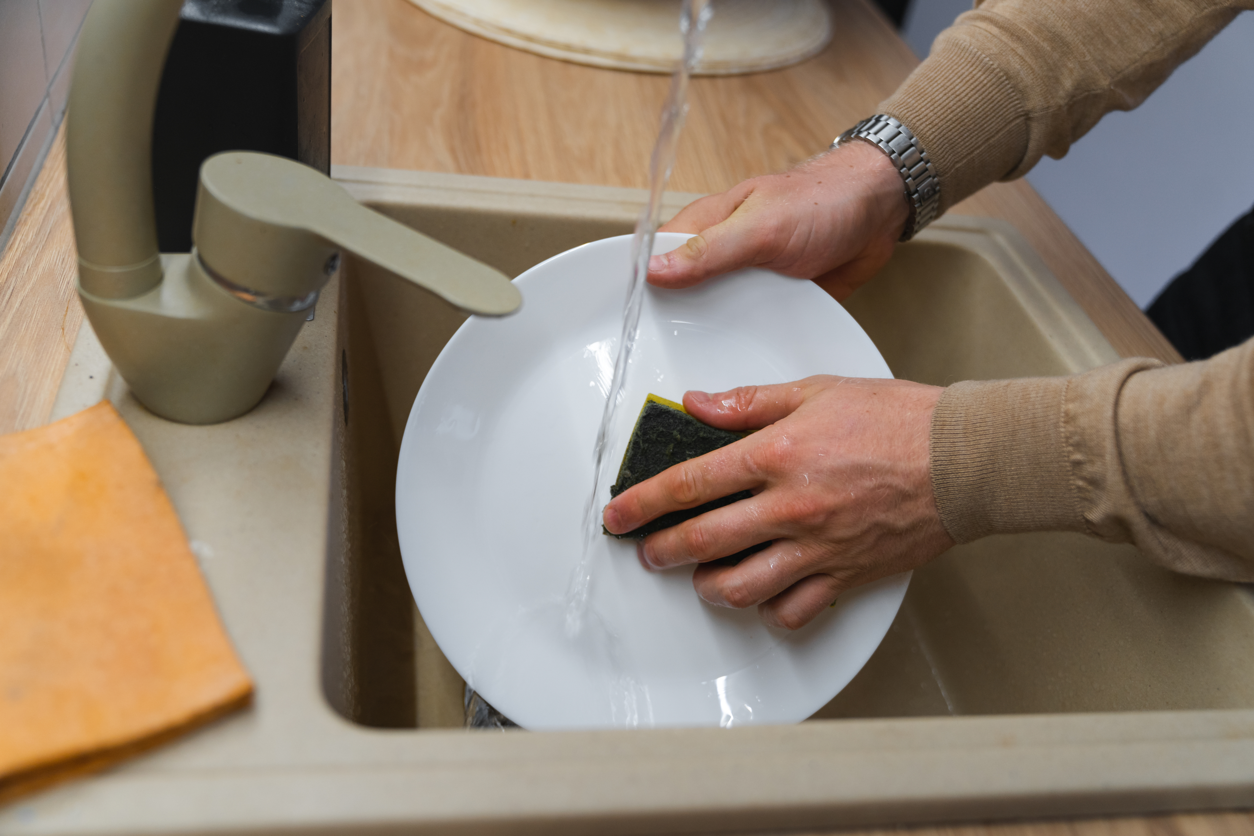 Close-up of a person washing a white plate with a sponge under running water in a kitchen sink