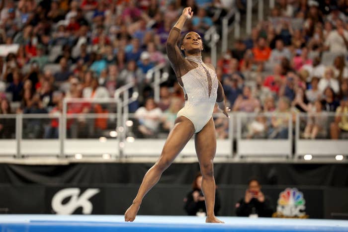 Simone Biles performs a floor routine at a gymnastics event, wearing a sparkling leotard, with a cheering crowd in the background