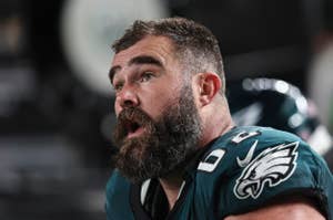 Jason Kelce, football player for the Philadelphia Eagles, shown during a game with a helmet off, wearing a team jersey, and looking to the side with an open mouth