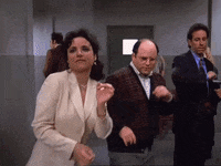 Elaine Benes, George Costanza, and Jerry Seinfeld dance energetically in a hallway scene from the TV show &quot;Seinfeld.&quot;