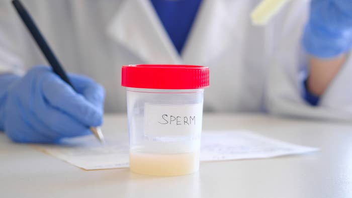Lab technician in gloves writes notes beside a labeled container of sperm on a table