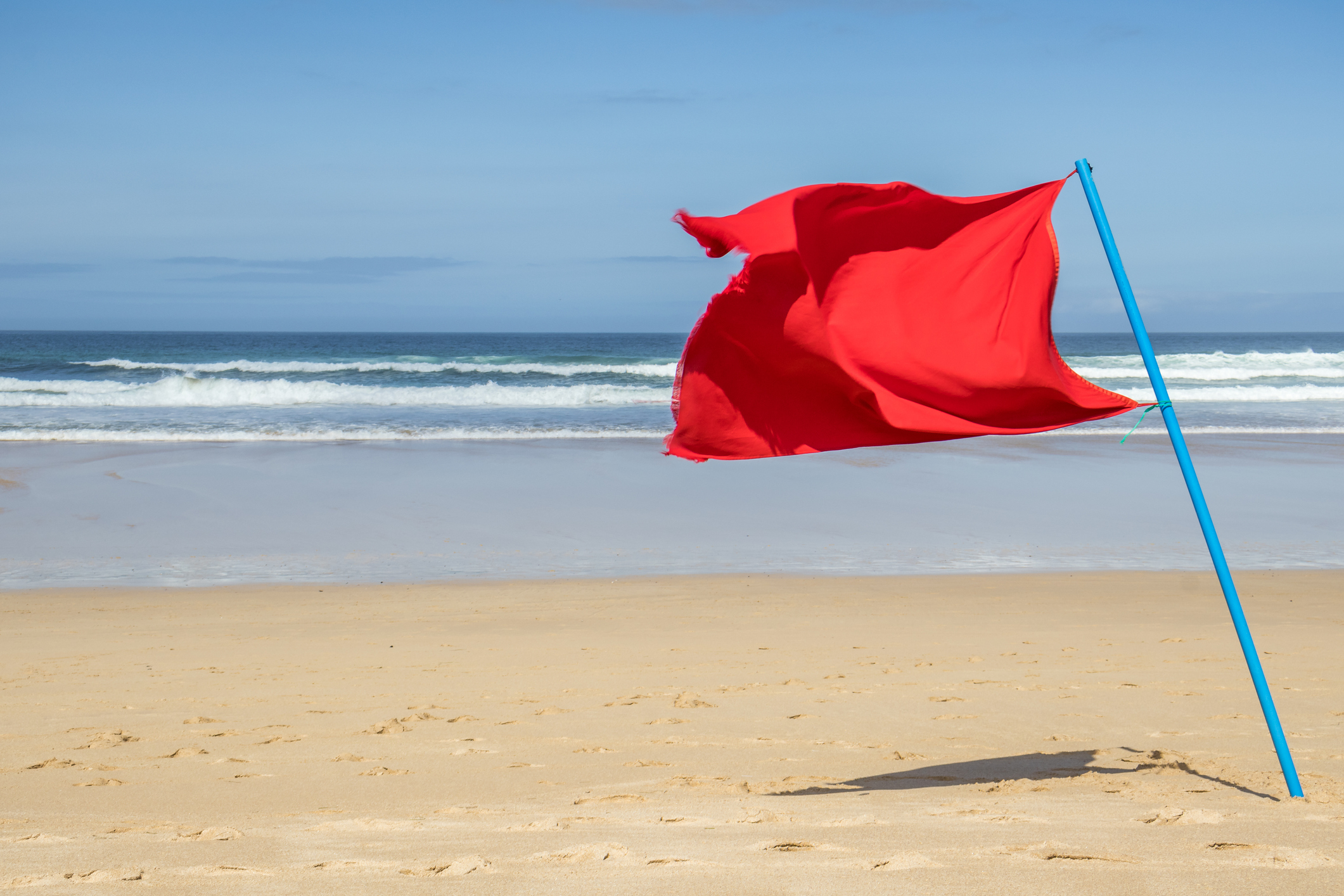 Red flag on a beach indicating a warning or danger, with waves in the background