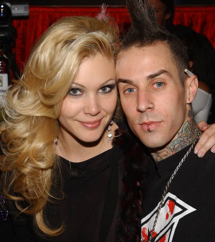 Shanna Moakler and Travis Barker pose together; Shanna wears a glamorous dress, while Travis sports a tattooed arm and a sleeveless top with a faux hawk hairstyle