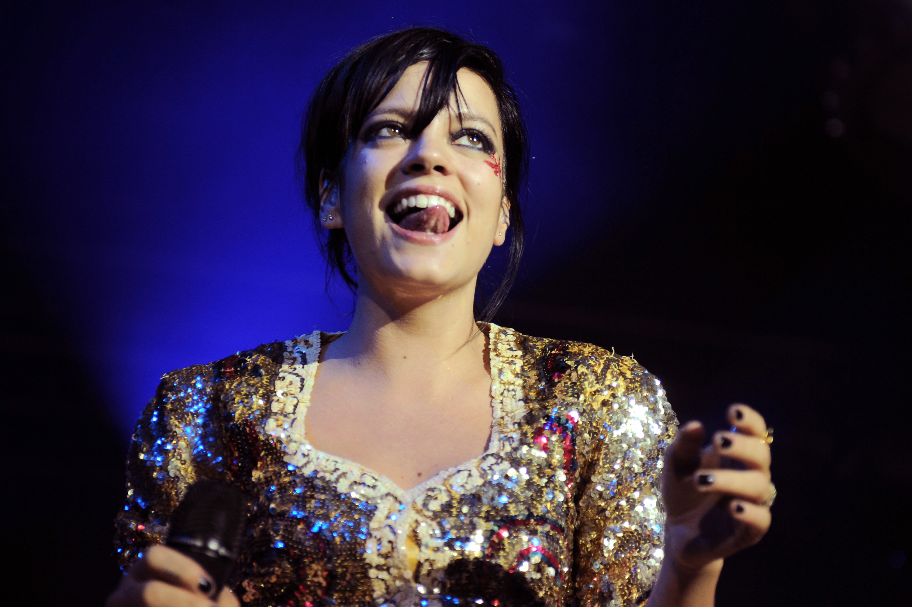 Lily Allen performs on stage, wearing a sparkly sequin dress