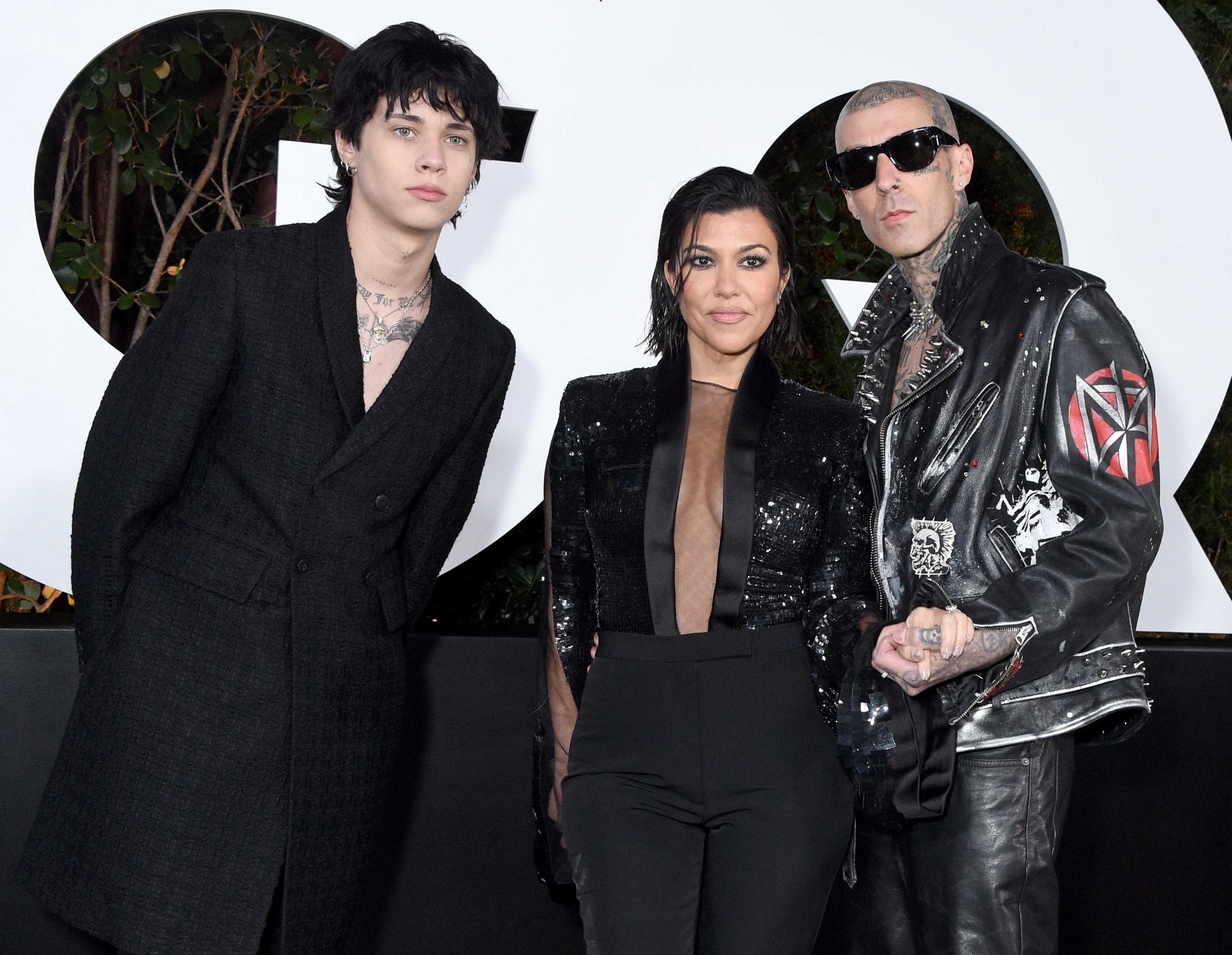 Landon Barker, Kourtney Kardashian, and Travis Barker pose on the red carpet. Landon and Kourtney wear black outfits, while Travis wears a leather jacket with patches