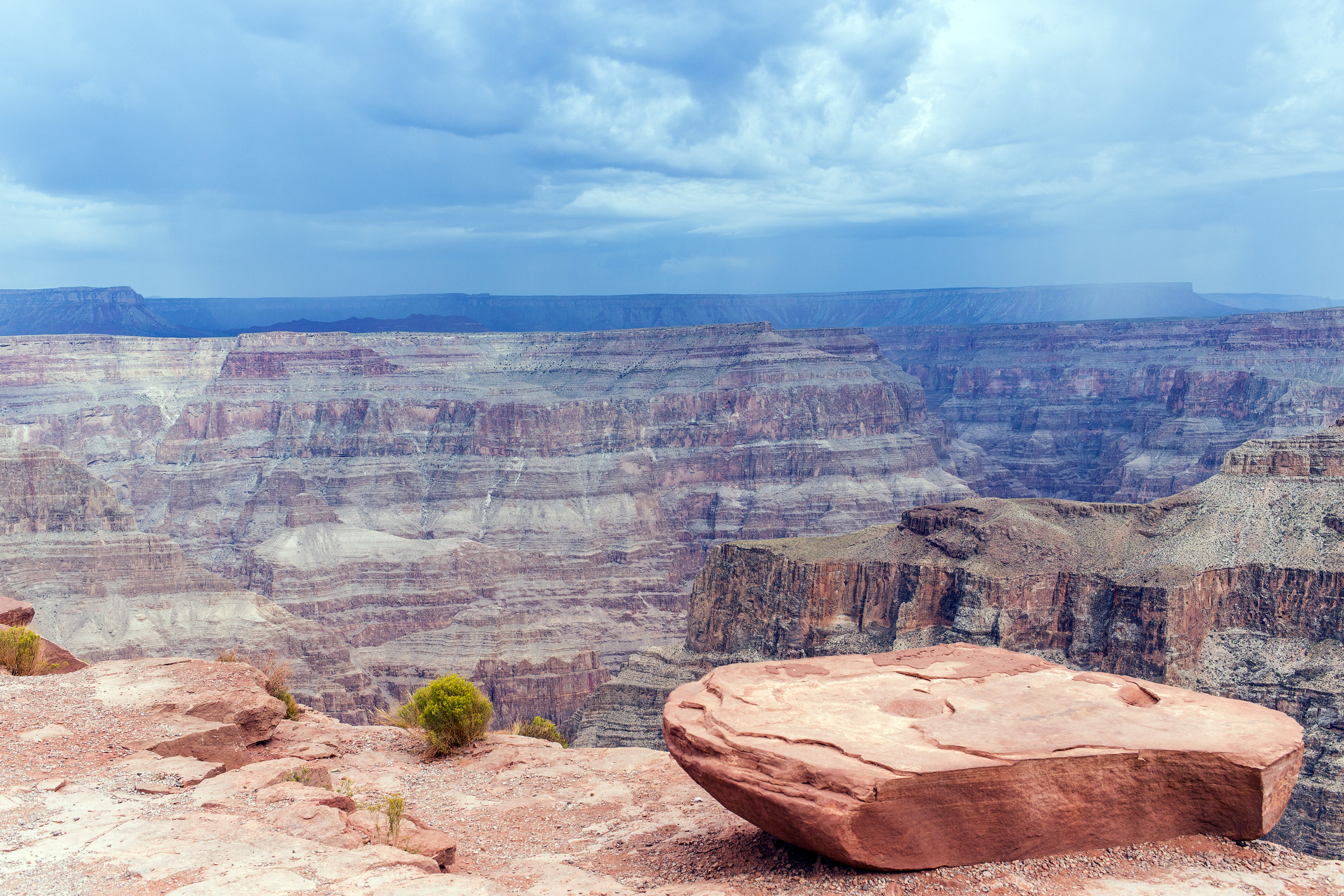 The image shows a breathtaking view of the Grand Canyon with layered rock formations and a large, flat rock in the foreground. No people are present