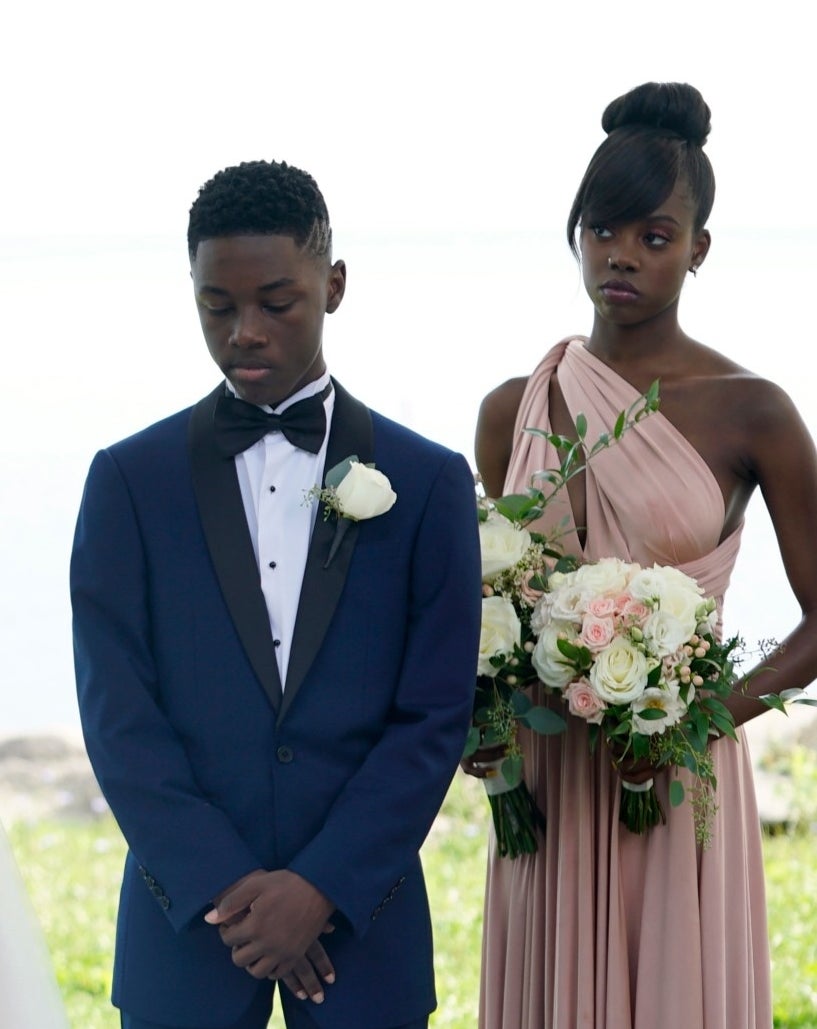 Wedding ceremony scene with two people exchanging vows, a child in a suit holding flowers, and a woman in formal attire with a bouquet. Names unknown