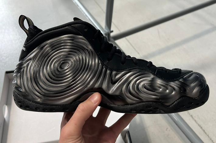 A hand holding a black sneaker with a distinctive swirling, textured design on the side
