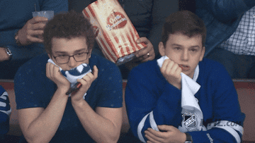 Two Toronto Maple Leafs fans looking disappointed at a hockey game, one holding a scarf, the other holding a towel