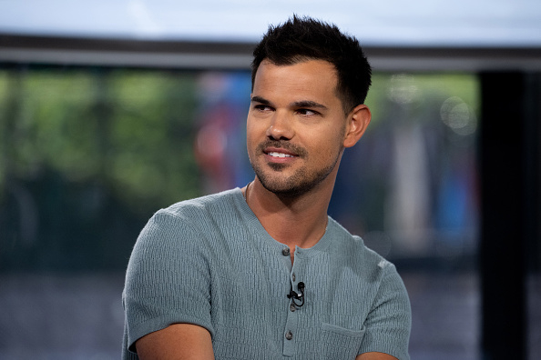 A person with short dark hair and a trimmed beard is wearing a textured short-sleeved shirt and smiling slightly, sitting in an indoor setting