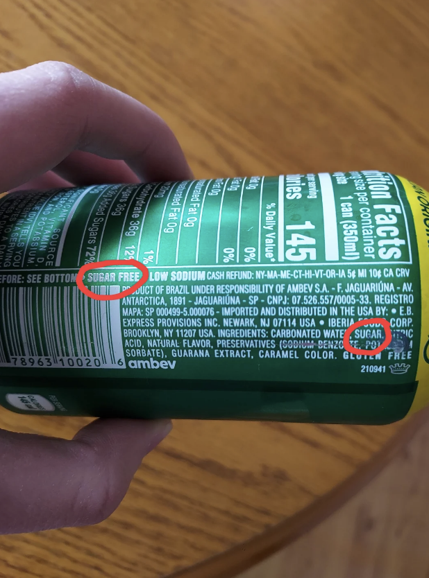 Can labeled 'Sugar Free' but also lists sugar in the ingredients. Close-up of a hand holding the can