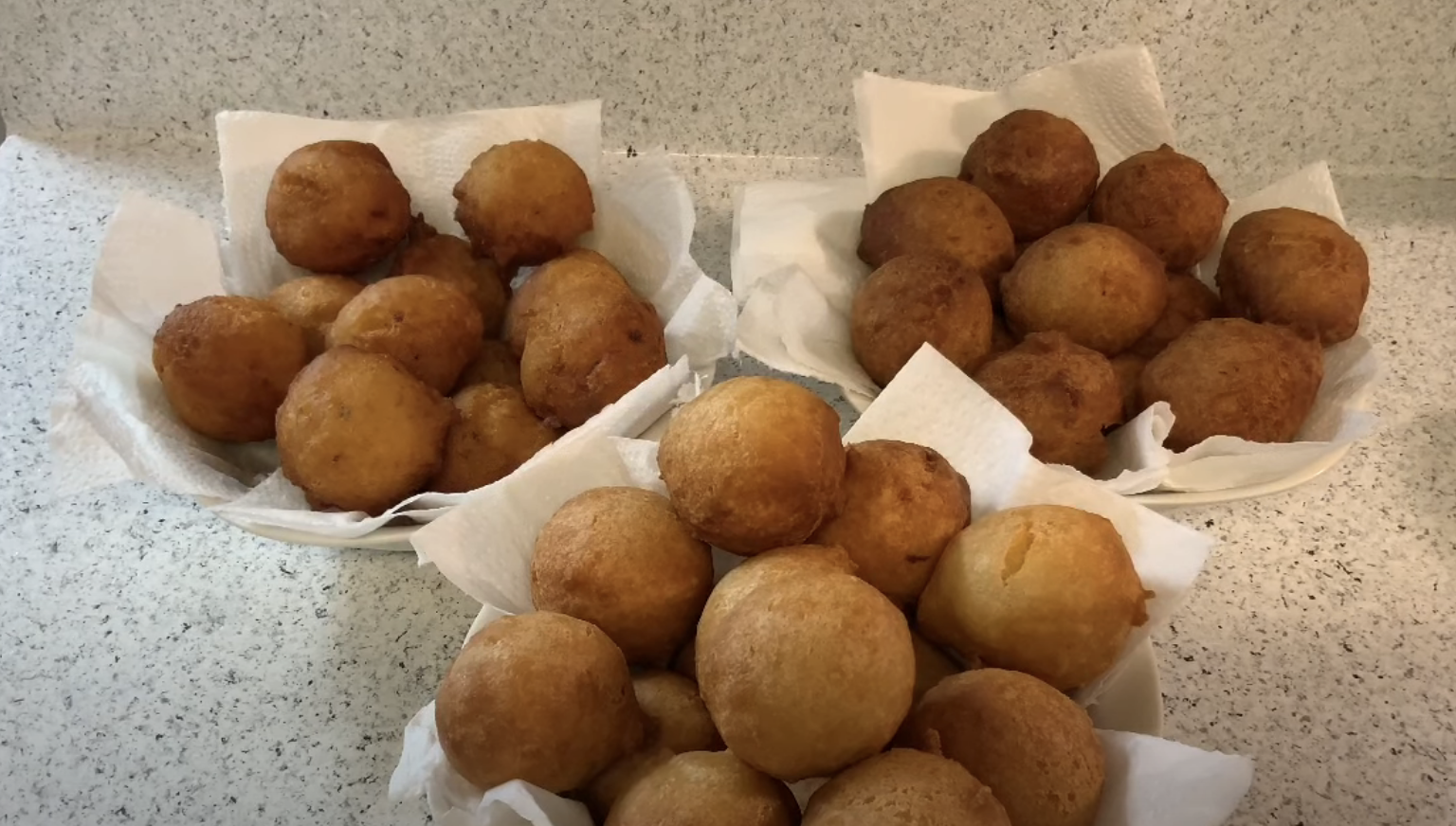 Four plates filled with round, golden-brown fried dough balls served on paper towels