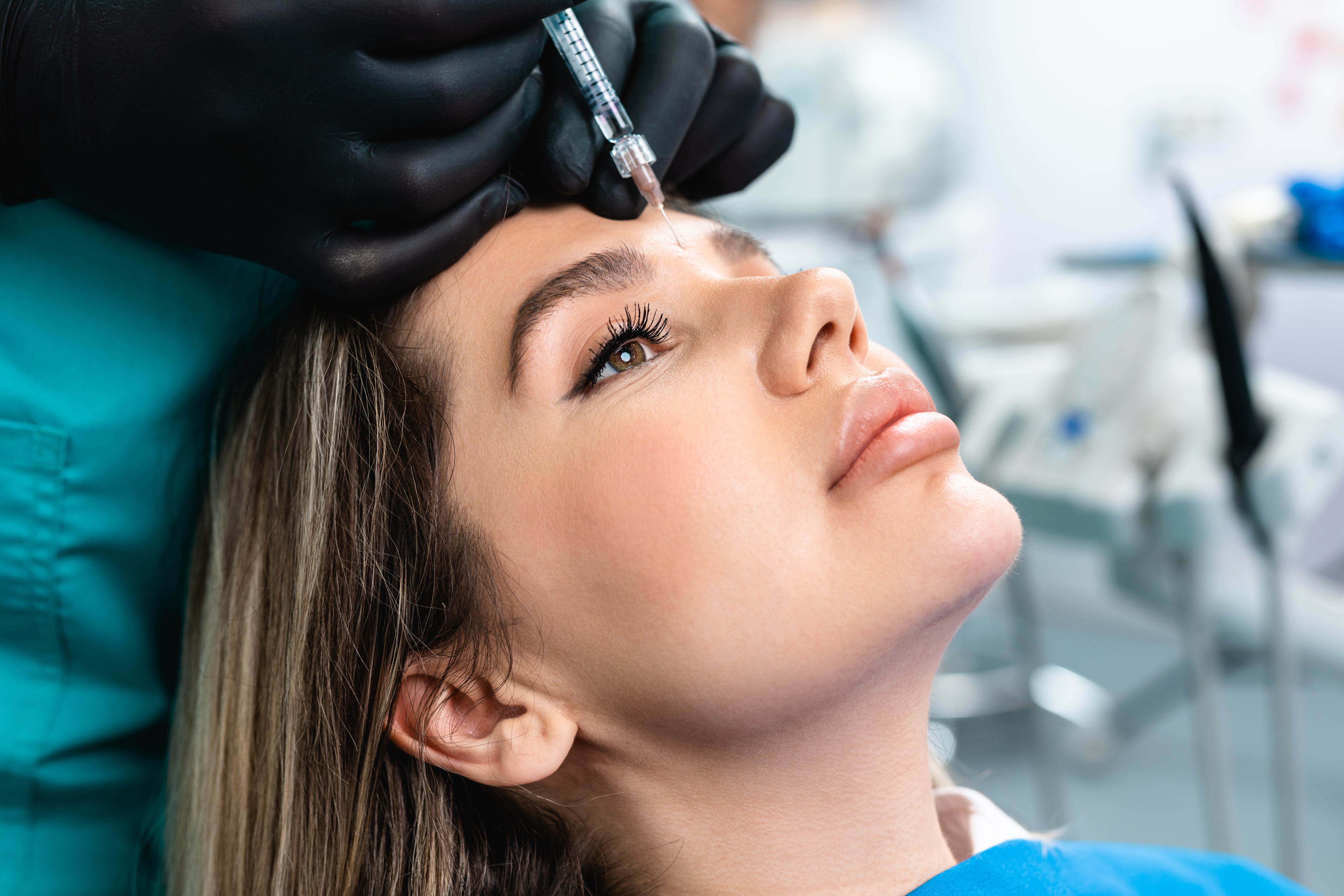 A woman receiving a cosmetic injection in her forehead at a medical clinic, given by a professional wearing gloves