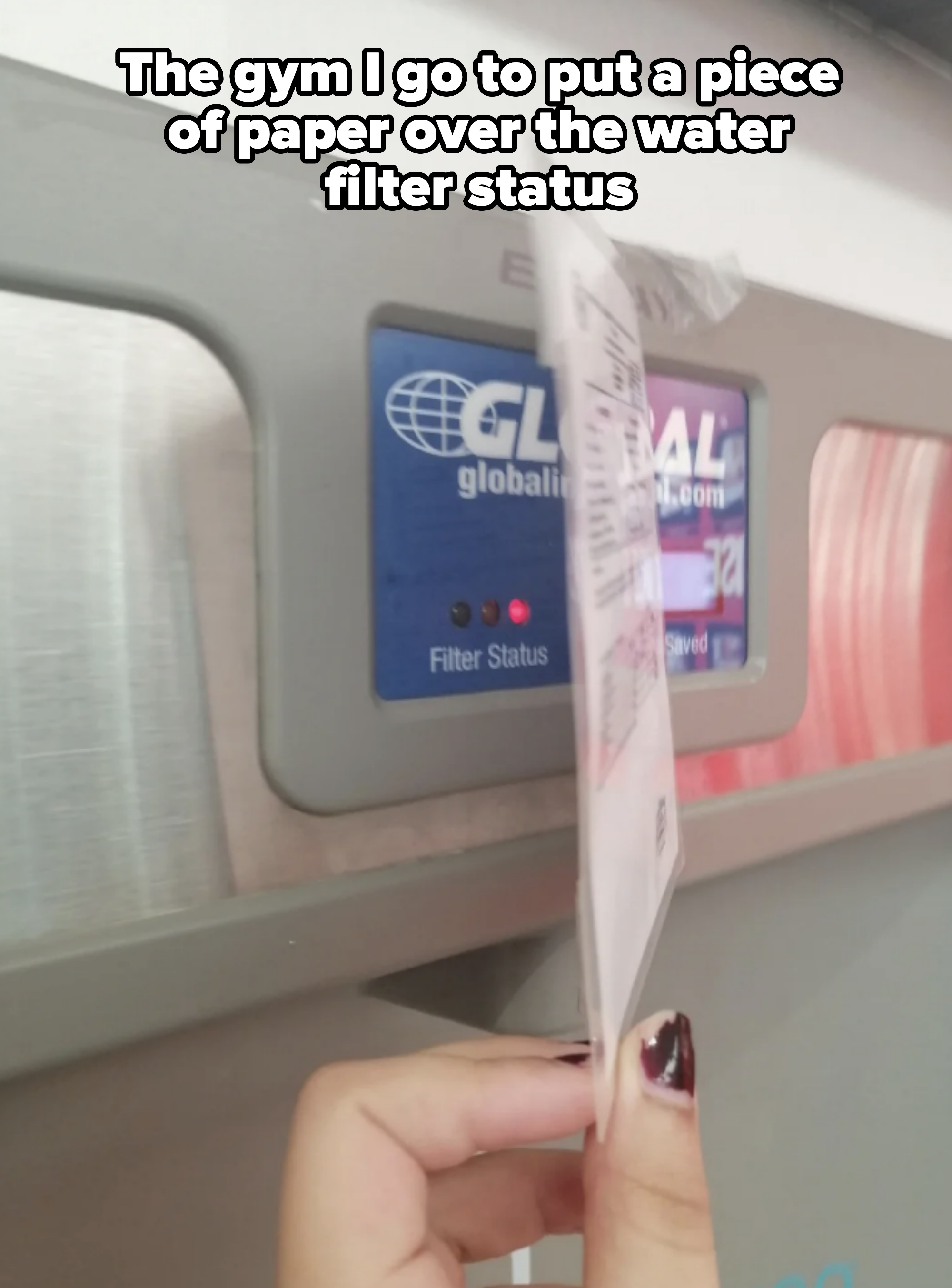 A person is holding a receipt in front of a screen displaying "Global" with a website URL, two lights labeled "Filter Status," and a part of a machine