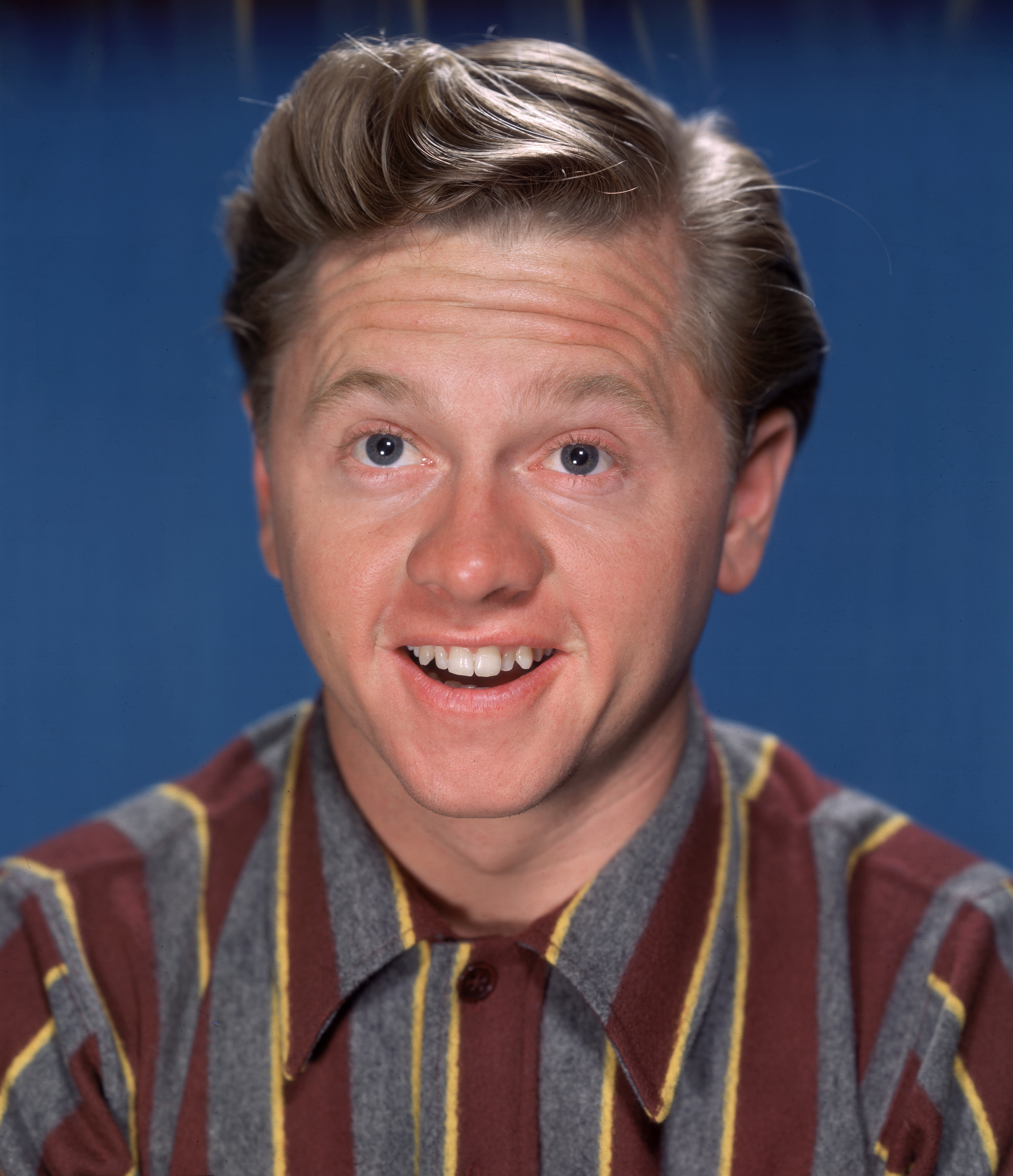 Mickey Rooney smiling, wearing a striped shirt, with a blue background