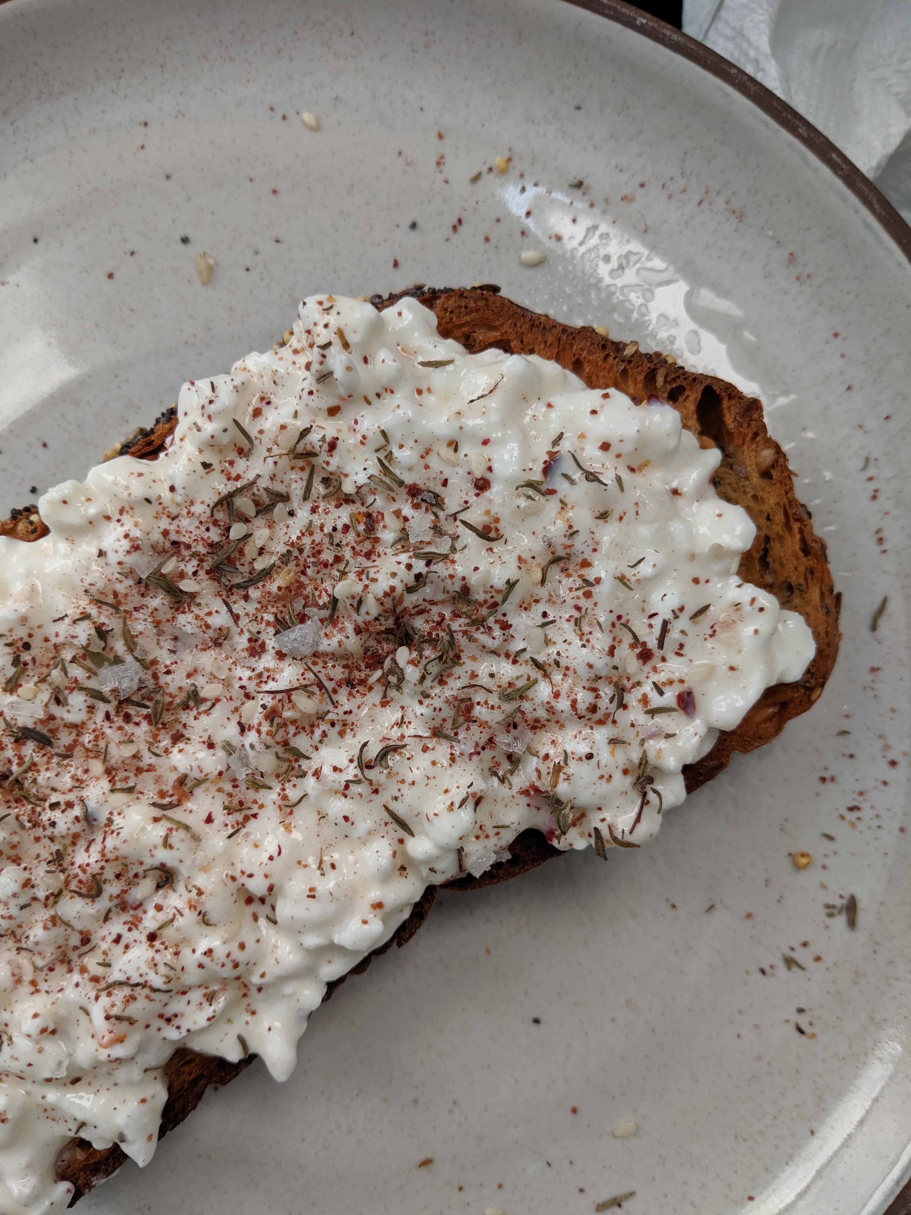 A plate with a slice of toast topped with cottage cheese and sprinkled with herbs and spices