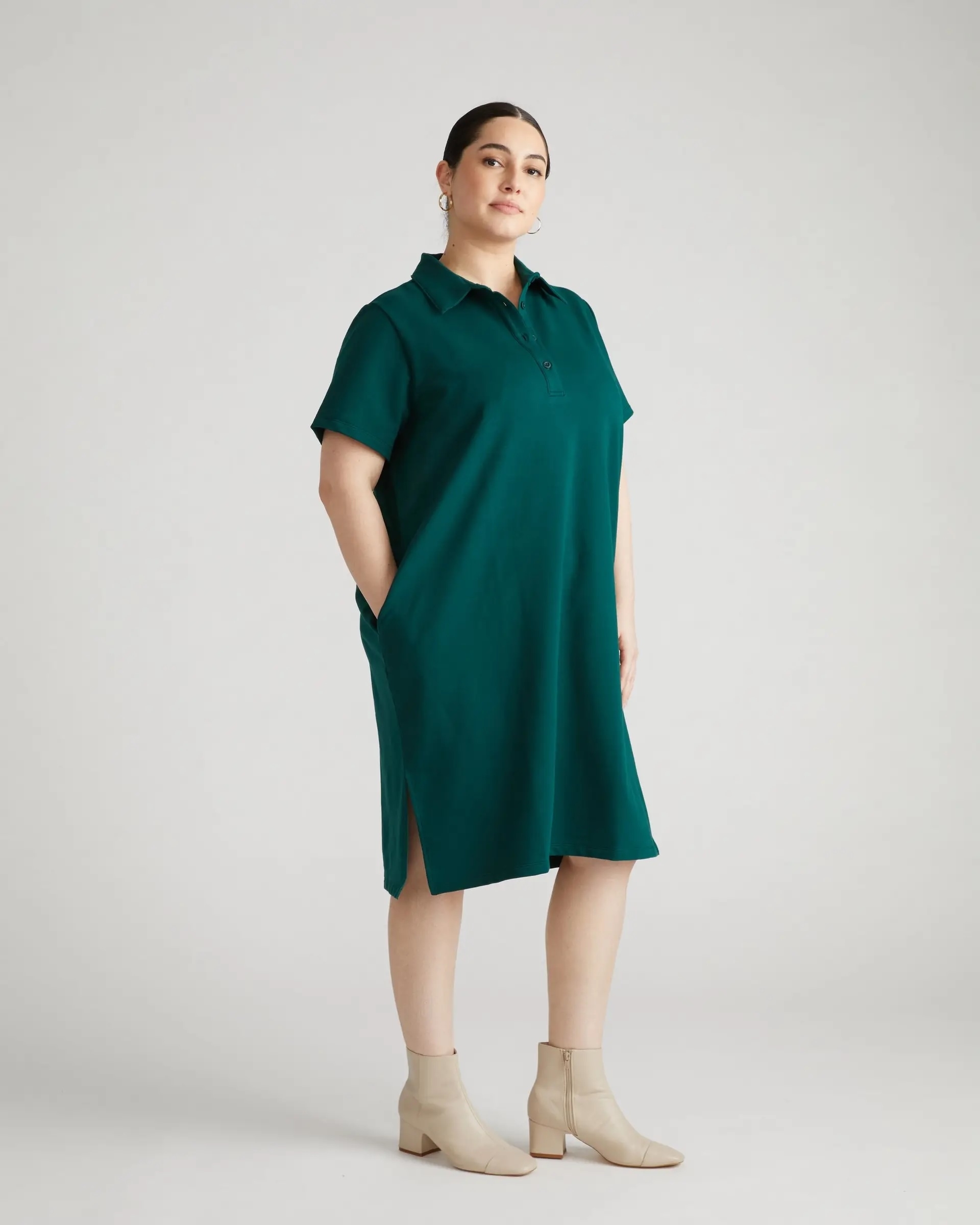 Woman modeling a teal short-sleeve, collared dress with pockets, paired with ankle boots