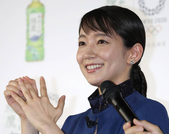 女性がイベントで話しています。背景にはオリンピックのロゴと緑茶のボトルが写っています。