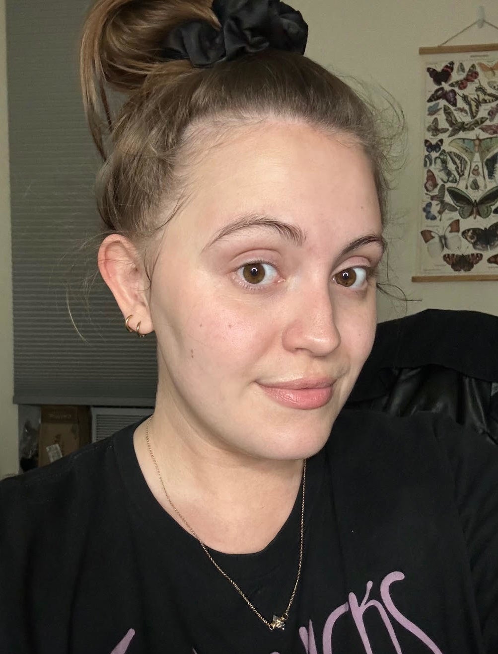 A woman with a high bun secured by a scrunchie, wearing a Stevies Nicks t-shirt, smiles at the camera. Background has butterfly artwork