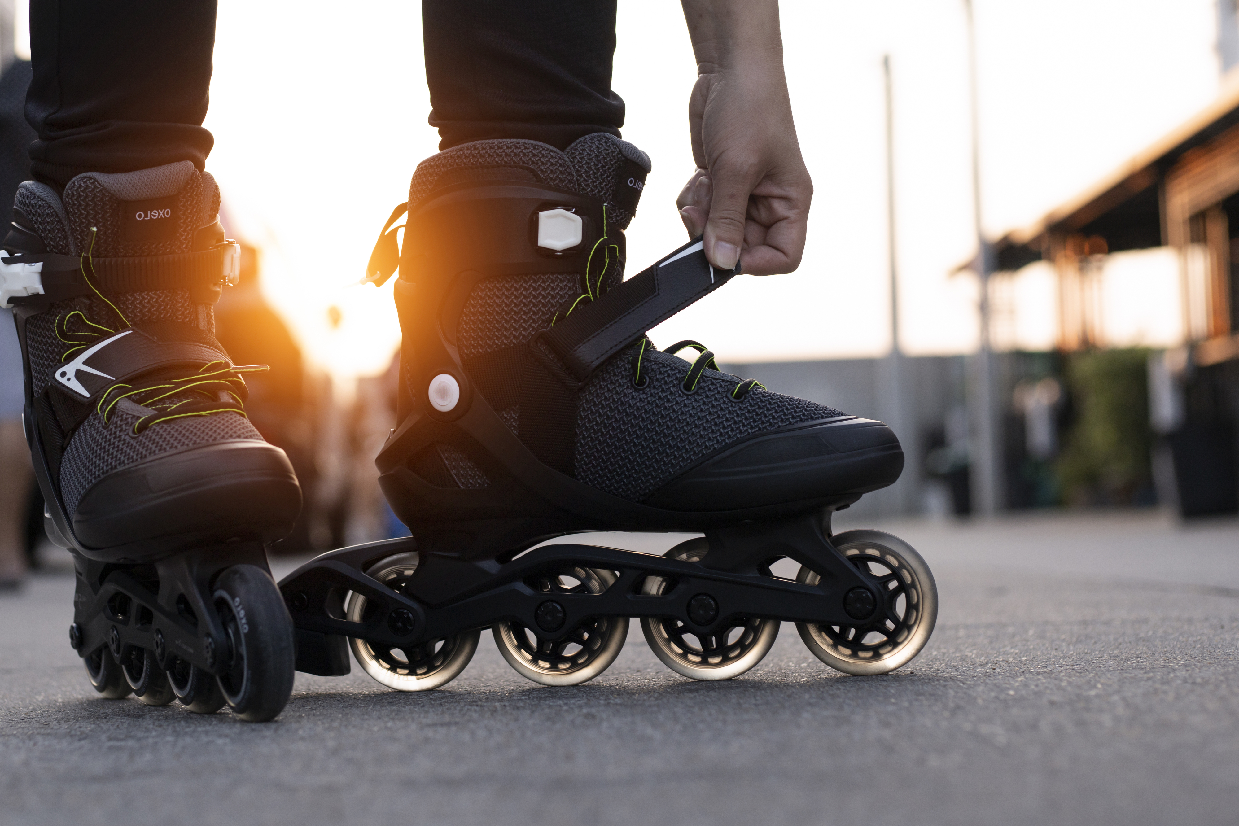 Person fastening inline skates on an outdoor pavement during sunset