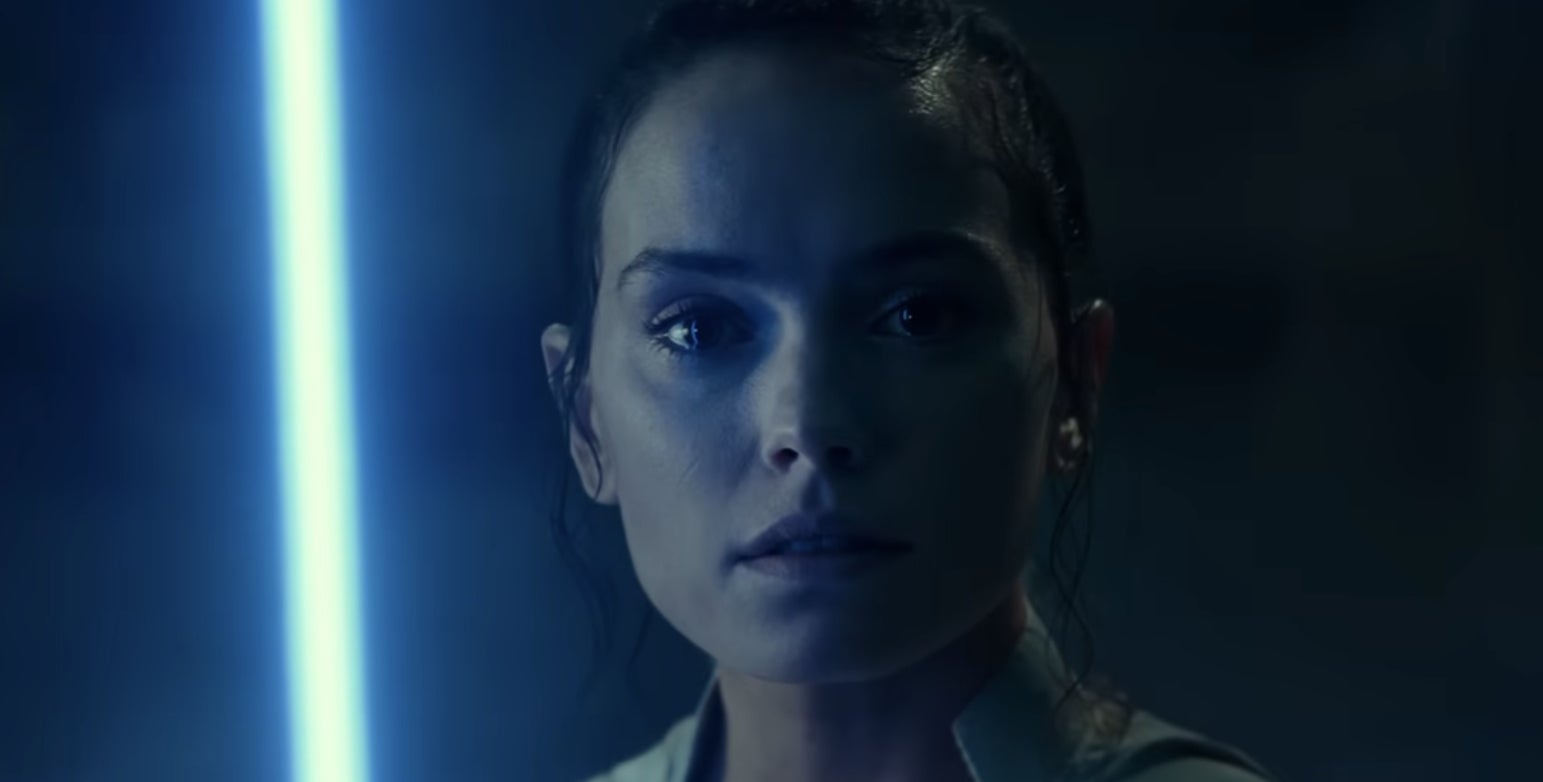 Daisy Ridley as Rey in a close-up shot where she is holding a blue lightsaber
