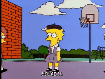 Lisa Simpson stands outside in a playground wearing a skirt and a beret, with text at the bottom that reads "You're it."