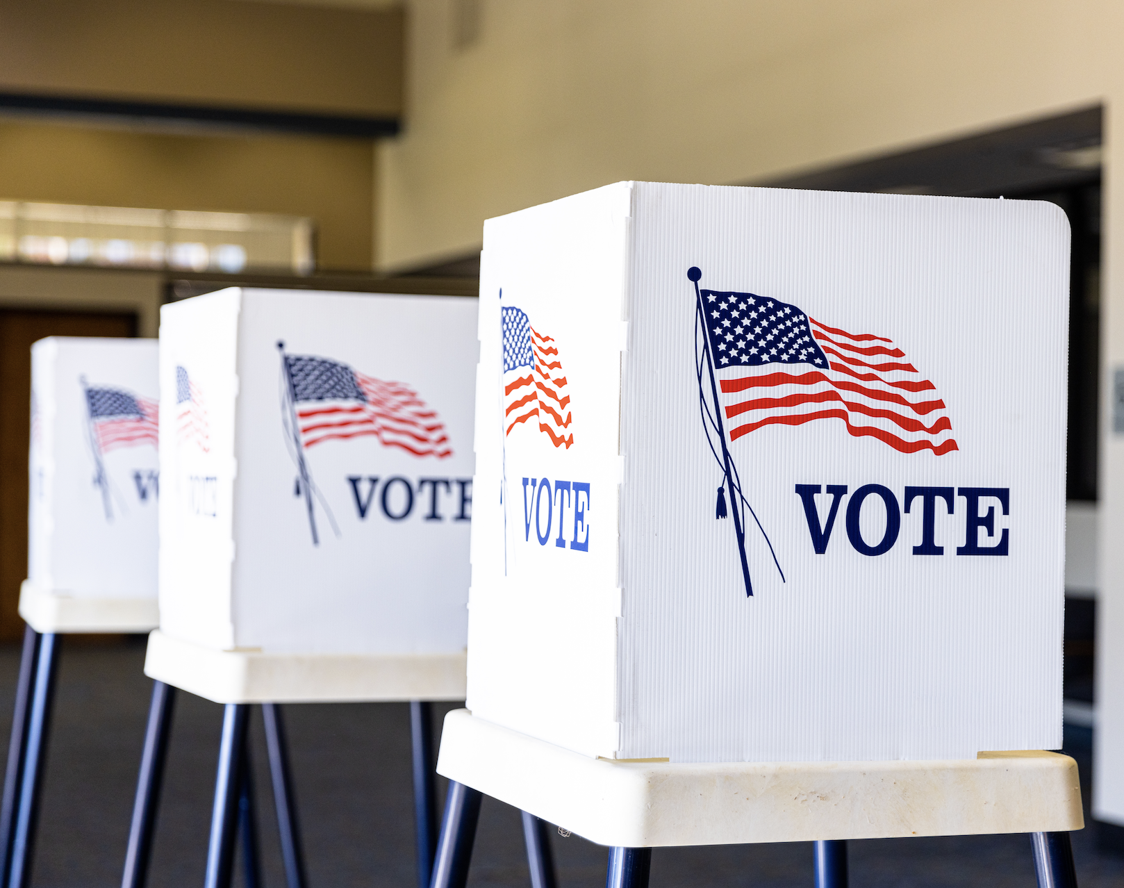 A row of voting booths with American flags and the word &quot;VOTE&quot; printed on them, set up in a large room