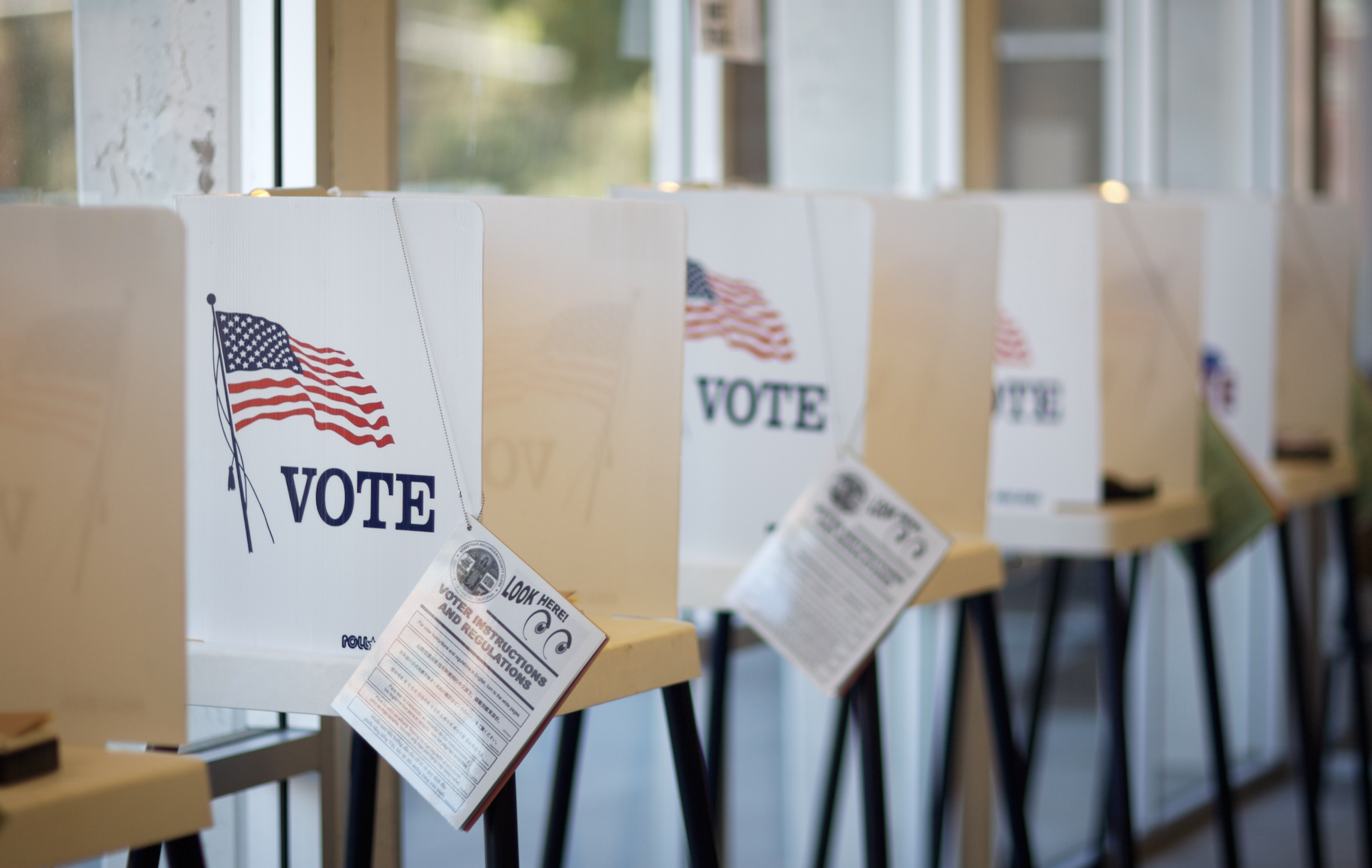 Voting booths with privacy shields displaying the word &quot;VOTE&quot; and an American flag are lined up in a row in a polling station