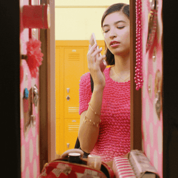 Teen girl stands by a locker talking on a smartphone while holding books in a school hallway