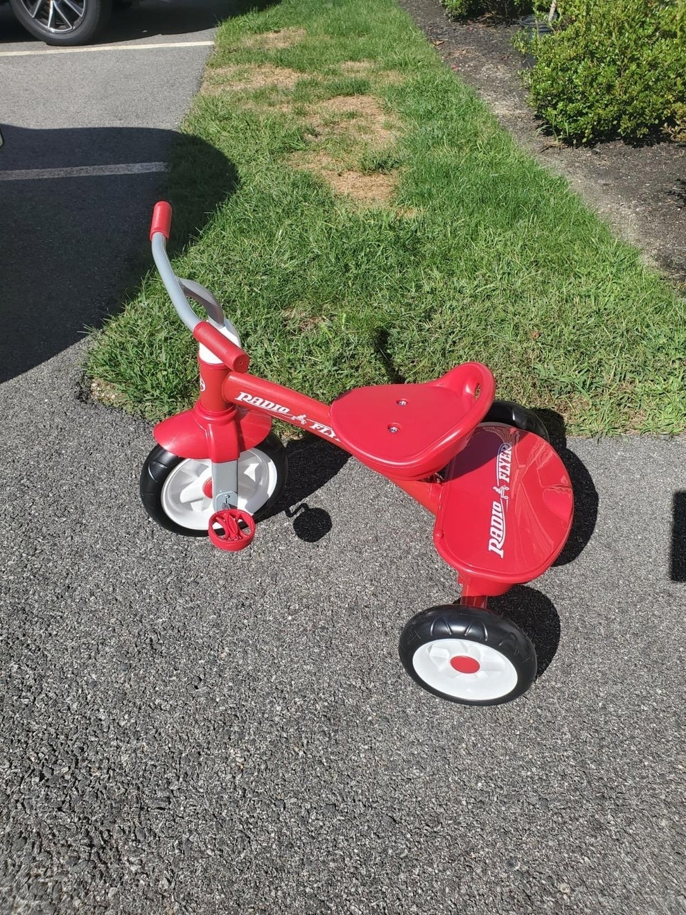 Red Radio Flyer tricycle with a gray handlebar, parked on a paved surface near grass