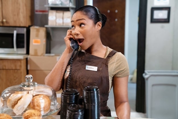 Tiffany Haddish on the phone while wearing a brown apron in a coffee shop/bakery setting