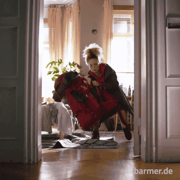 A woman struggles to carry a large red backpack in a living room setting, indicative of heavy packing or moving. The text "barmer.de" is visible on the bottom right
