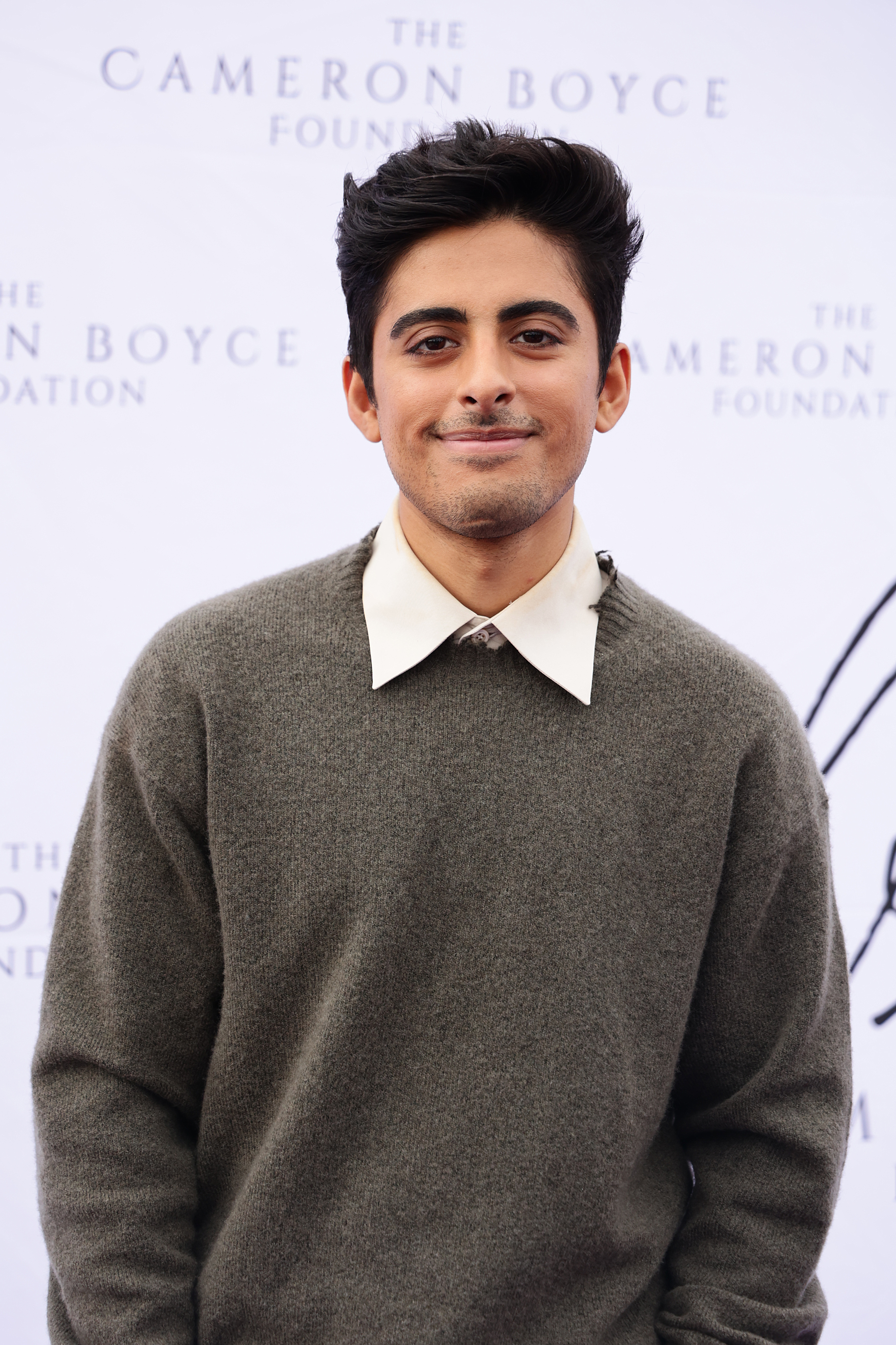 Karan Brar at The Cameron Boyce Foundation event, wearing a white shirt under a gray sweater, smiling at the camera