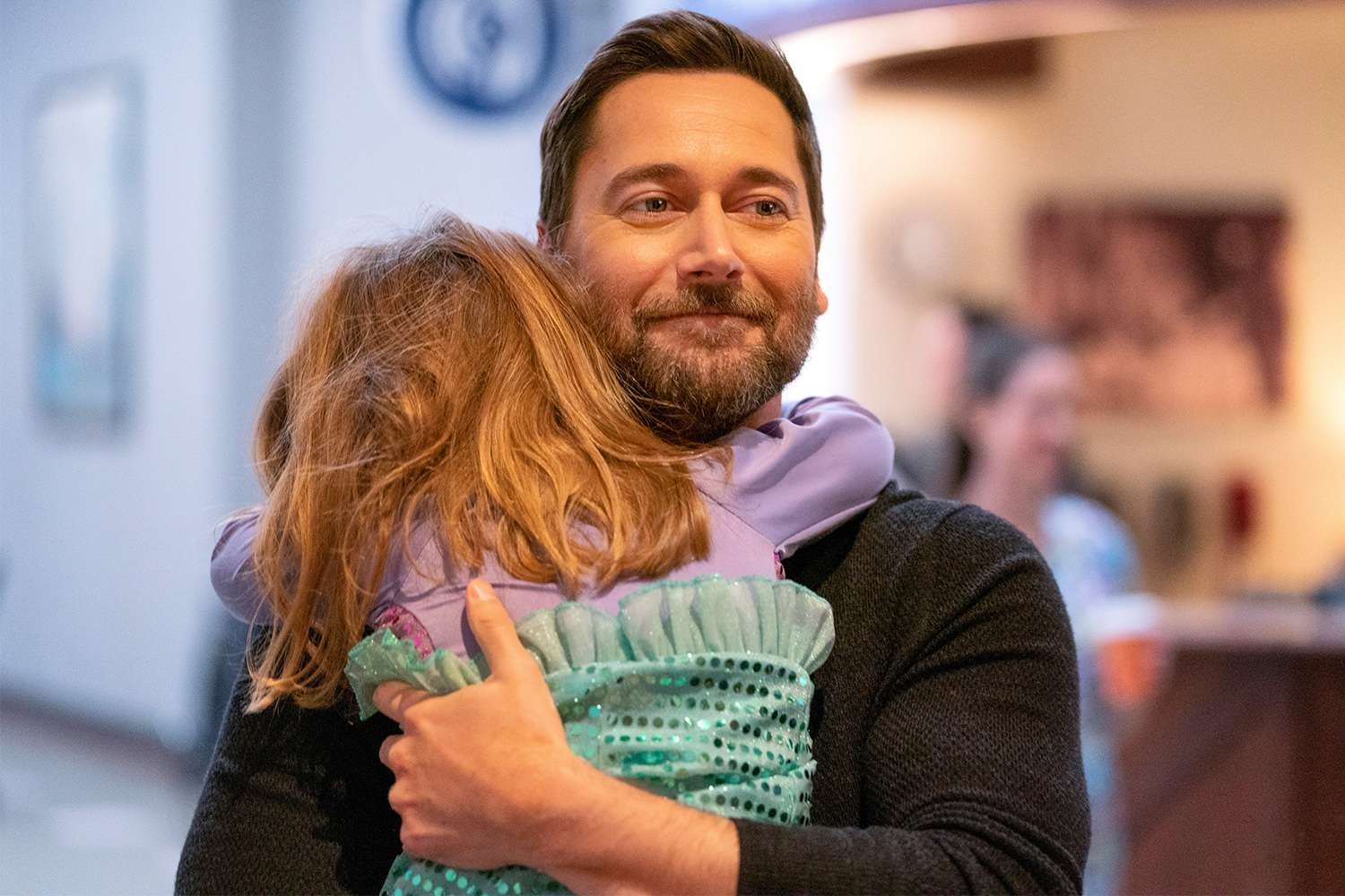 Ryan Eggold from 'New Amsterdam' hugs a young girl inside a building