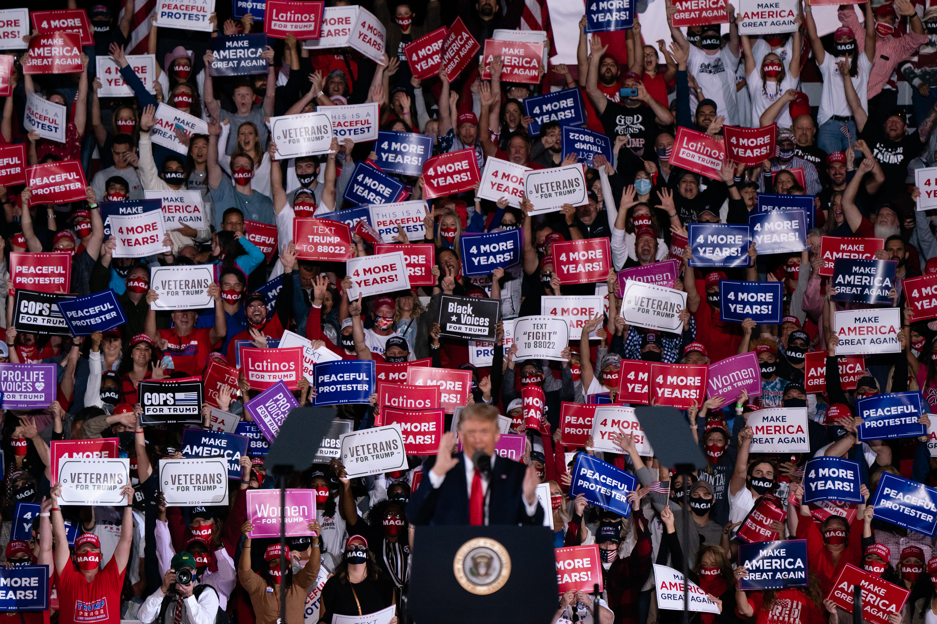Donald Trump at a political rally surrounded by people holding signs