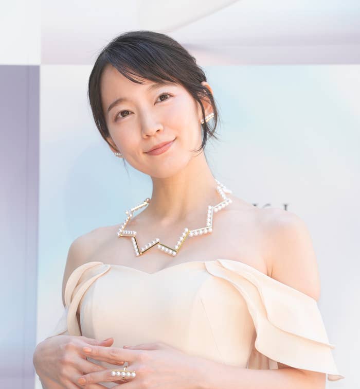 白いオフショルダードレスを着た女性が優雅に微笑む。