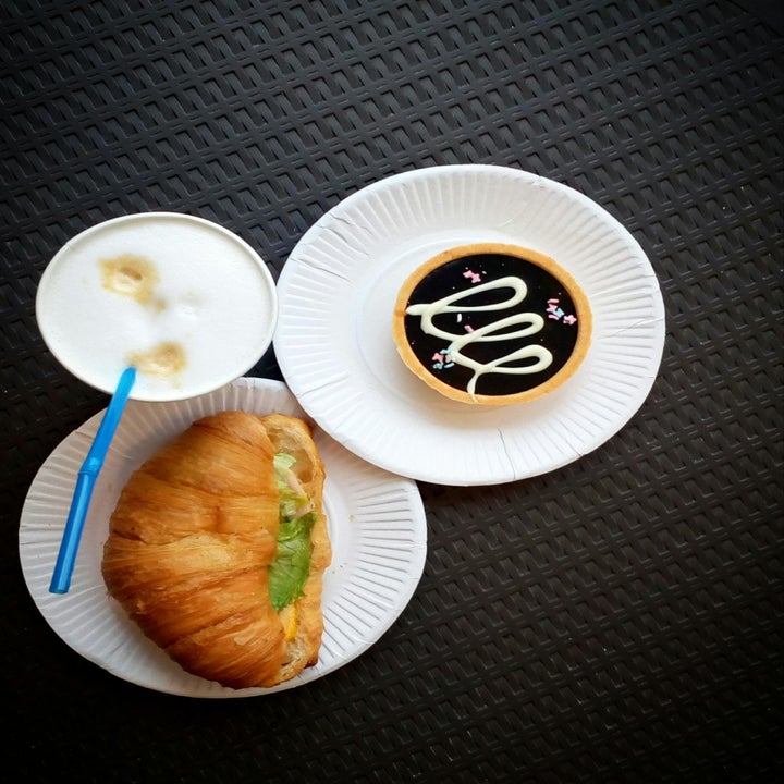 A plate with a croissant and a small salad, a cup of frothy coffee with a blue straw, and a pastry with decorative icing on separate plates