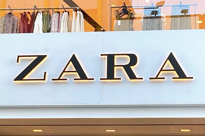 Storefront sign displaying &ldquo;ZARA&rdquo; with a glimpse of clothing items visible through the window