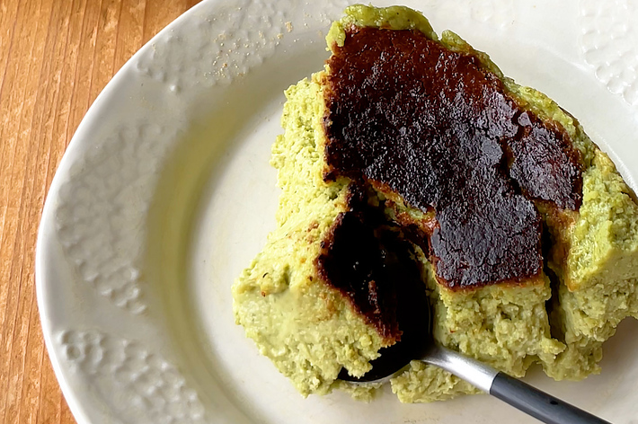 皿の上に盛られたピスタチオ風味のバスクチーズケーキのクローズアップ。フォークが添えられています。